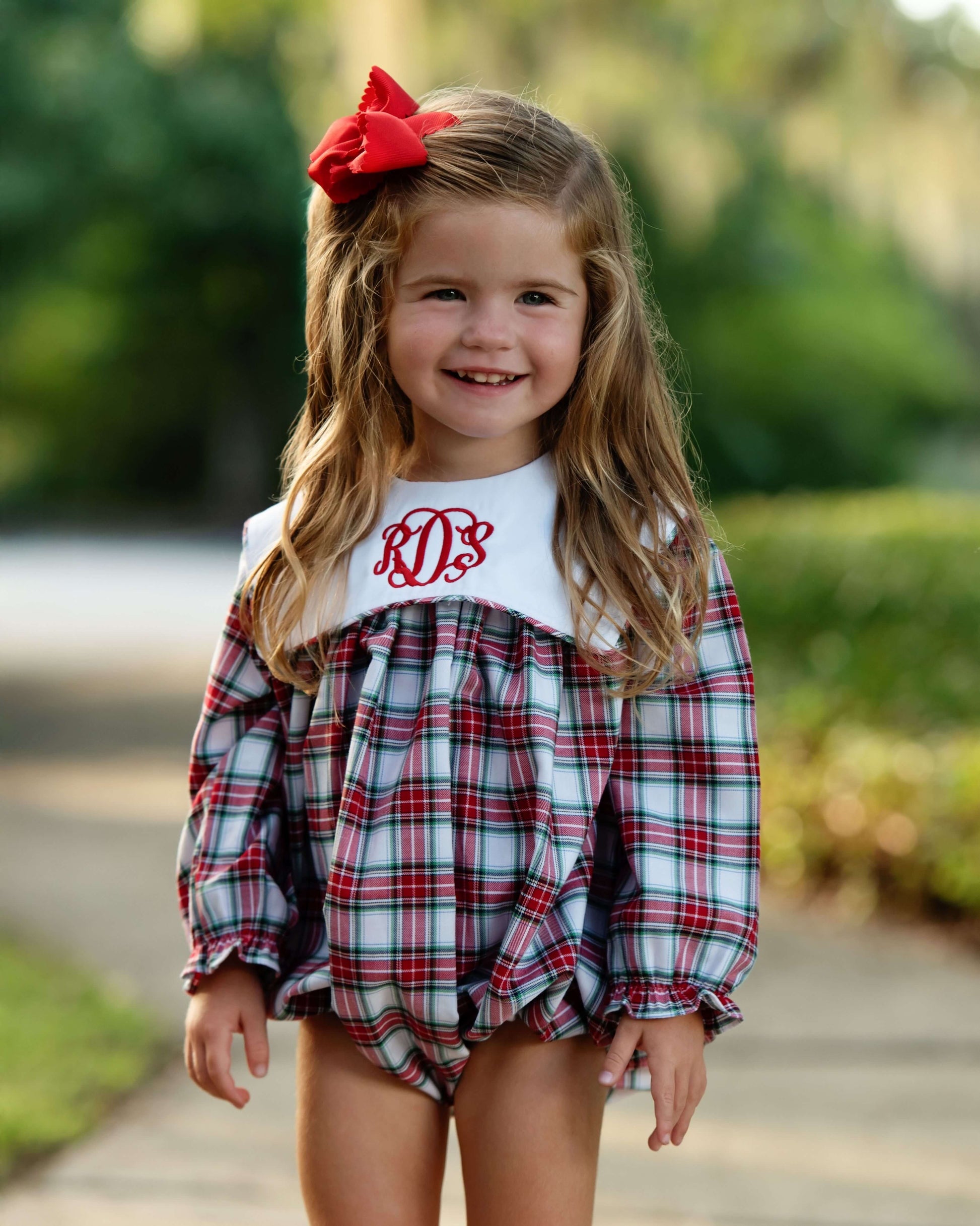 Young girl wearing a plaid outfit with a red bow outdoors