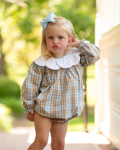 Young girl wearing a plaid shirt with a large white collar outdoors.