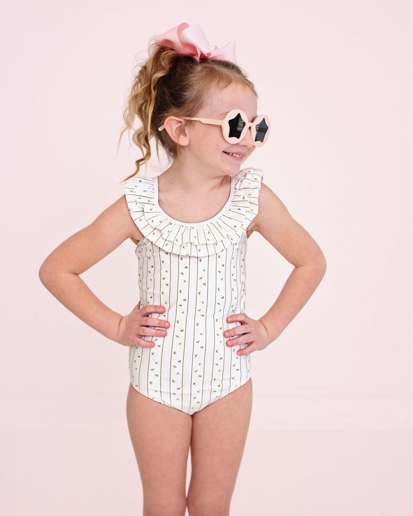 Young girl wearing a polka dot swimsuit with a ruffled collar on a pink background