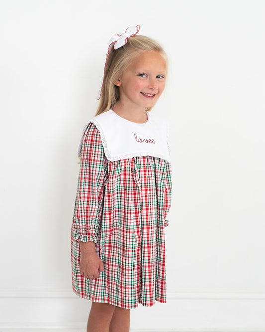 Young girl wearing a red and green checkered dress with a white collar on a white background