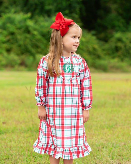 Young girl wearing a red and green plaid nightgown with a large red bow in a grassy field.
