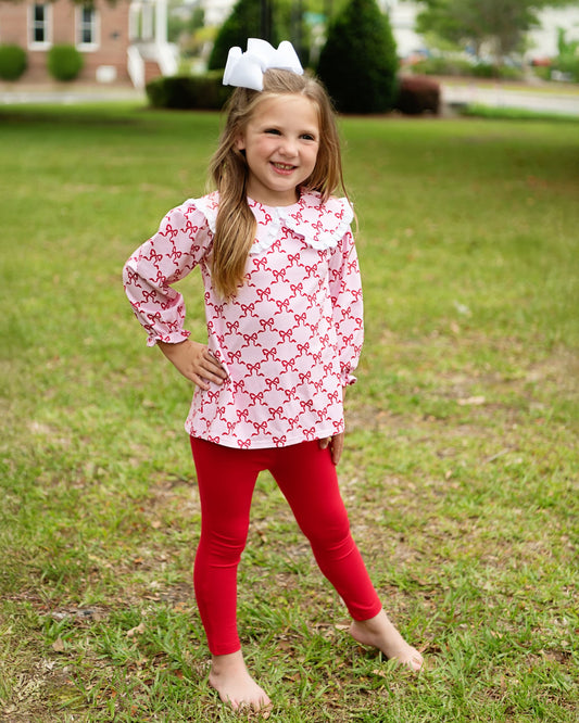 Young girl wearing a red and white patterned top and red leggings standing on grass.