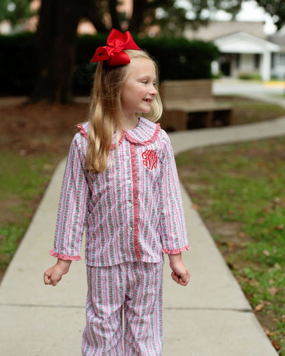 Young girl wearing a red and white striped pajama set with a large red bow in her hair, standing on a sidewalk.