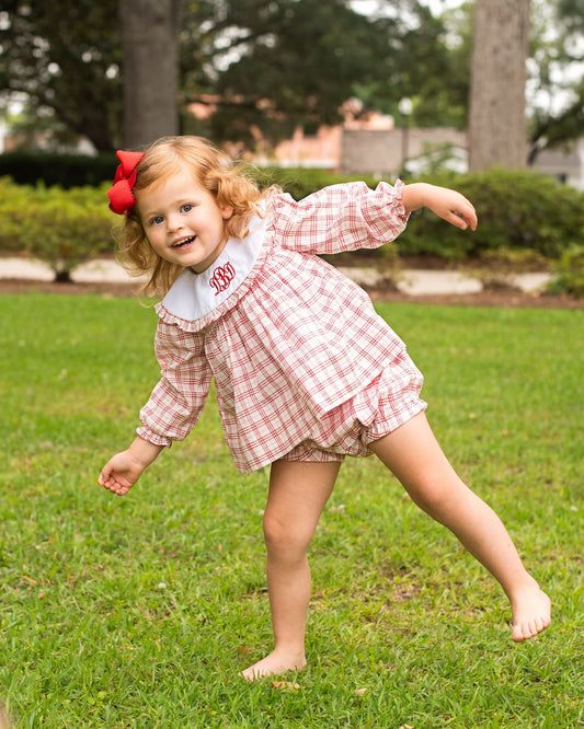 Young girl wearing a red plaid outfit standing on one leg on the grass
