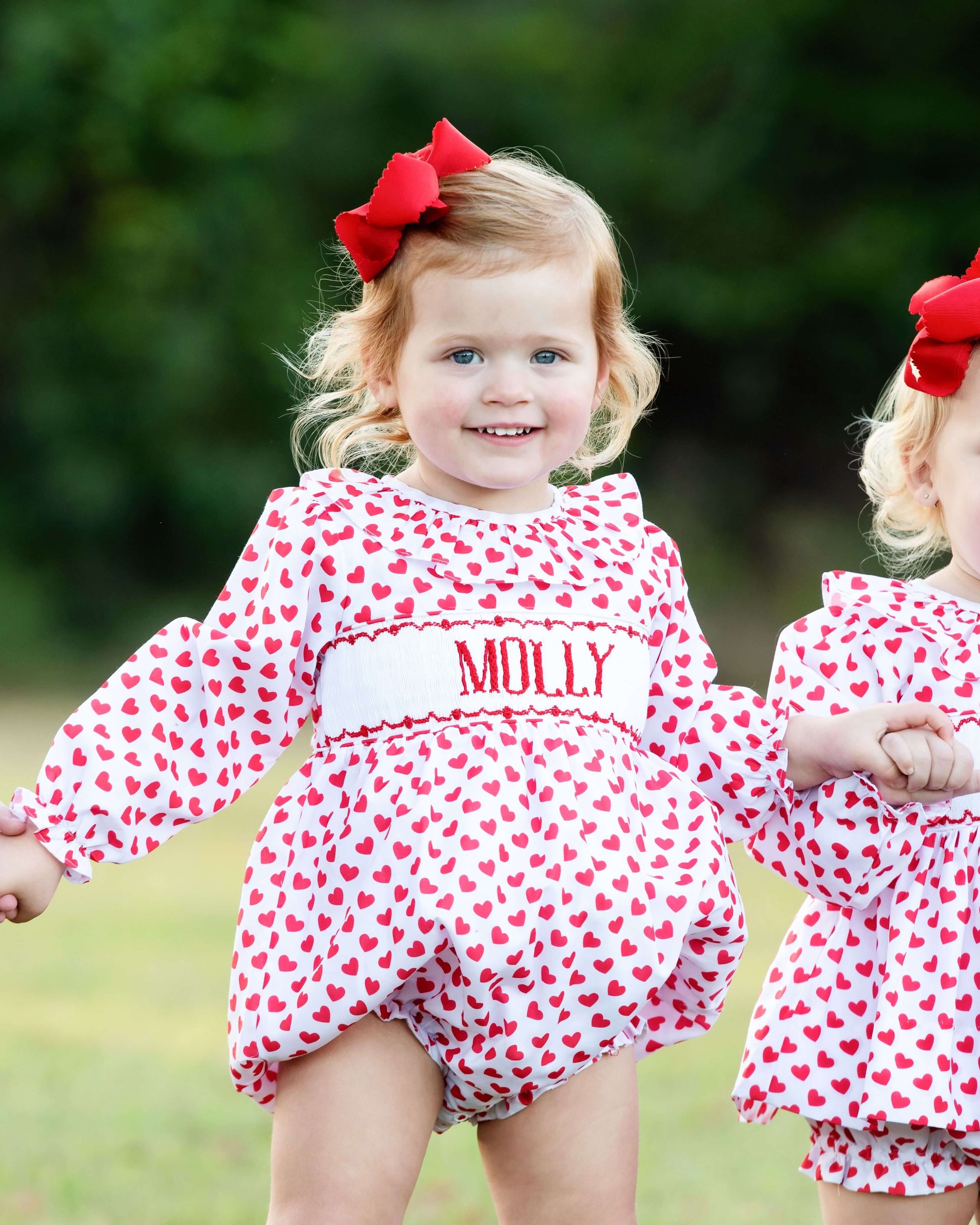 Young girl wearing a red valentine smocked bubble standing in a blurred field