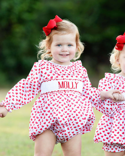 Young girl wearing a red valentine smocked bubble standing in a blurred field
