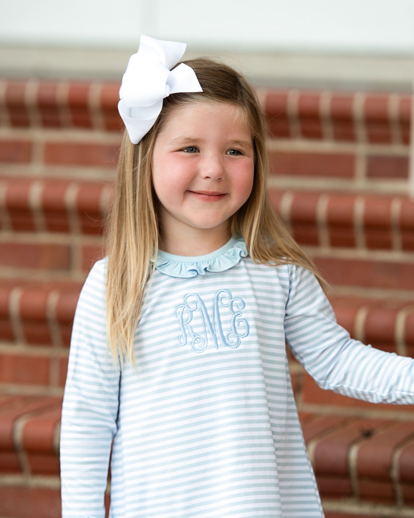 Young girl wearing a striped dress with a white bow in front of brick steps