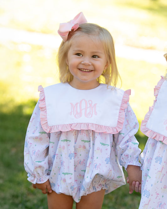 Young girl wearing a white blouse with pink ruffled collar and floral design outdoors.