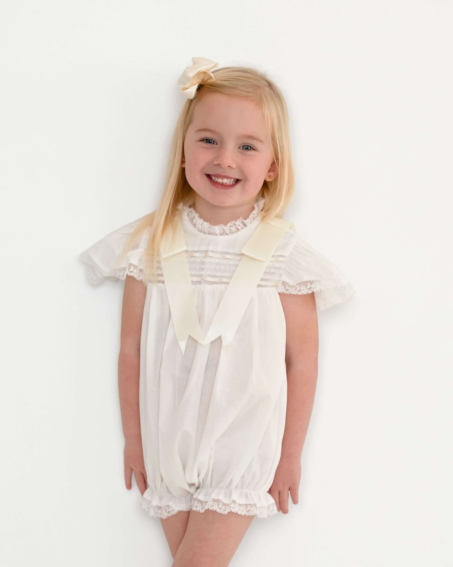 Girl wearing ivory satin bubble romper with large bow accessory, studio portrait
