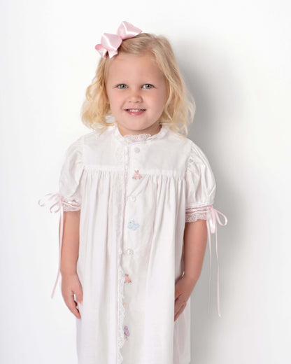 Young girl wearing a white dress with pink accents against a plain background
