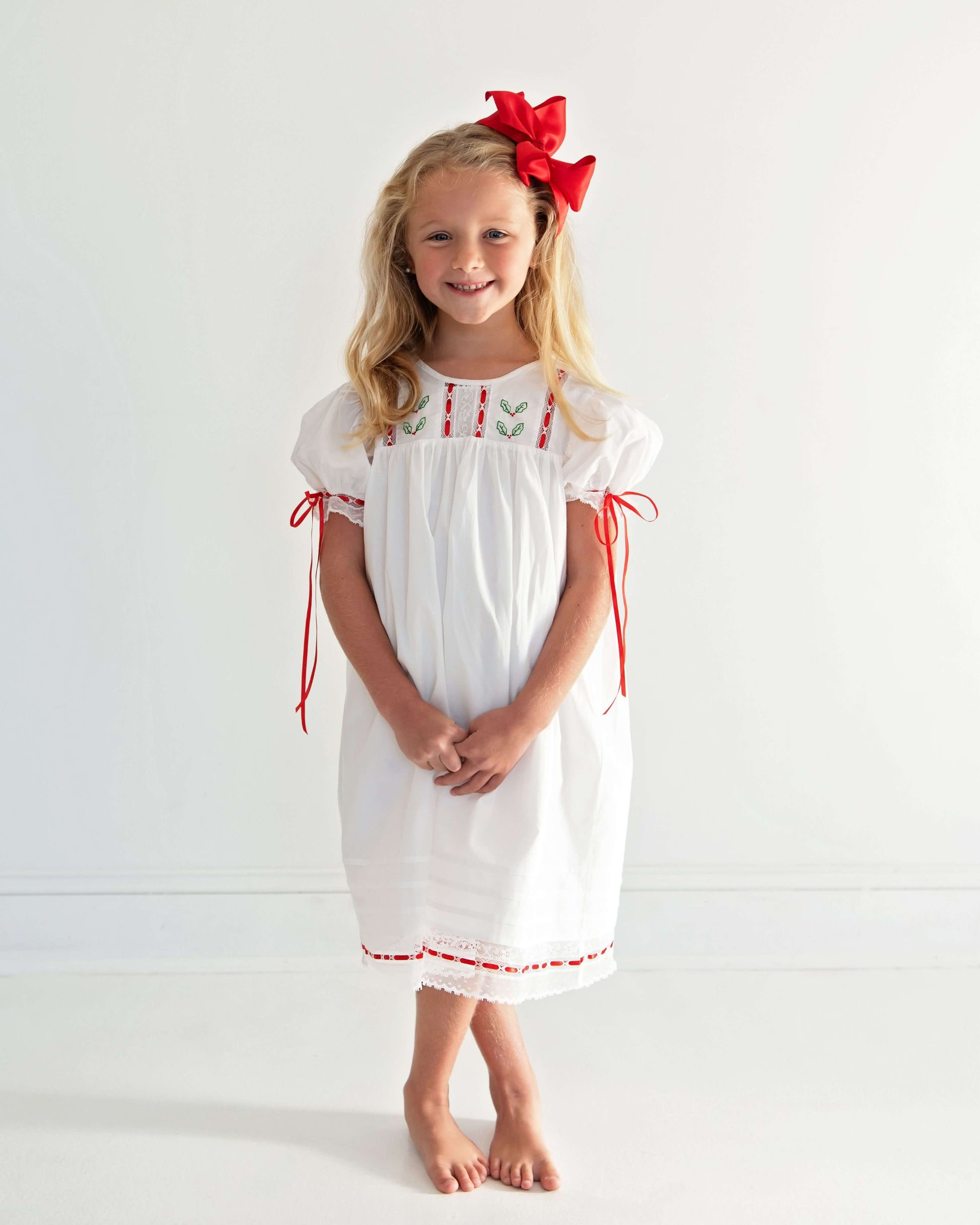 Young girl wearing a white dress with red accents and a red bow in her hair against a white background