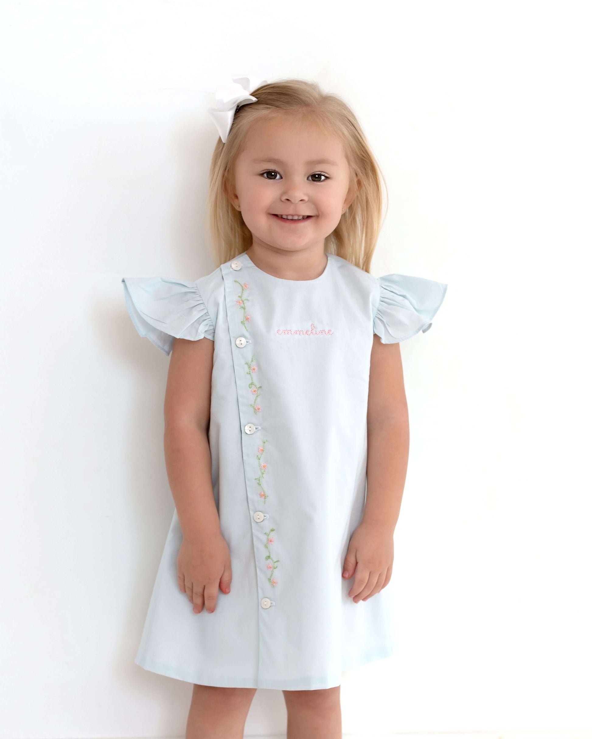 Young girl wearing a white dress with ruffled sleeves on a plain background