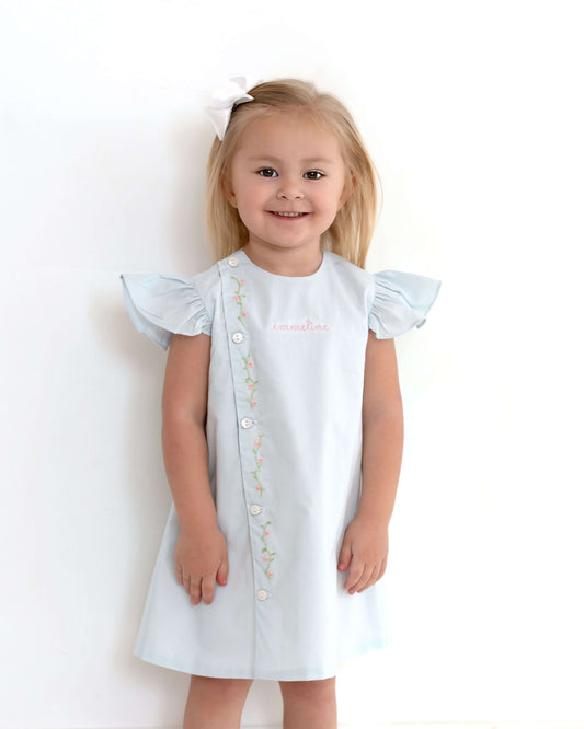 Young girl wearing a white dress with ruffled sleeves on a plain background