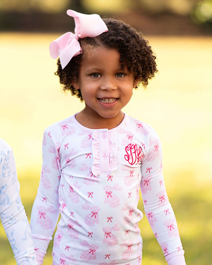 Young girl wearing a white long-sleeve shirt with pink bow patterns outdoors.