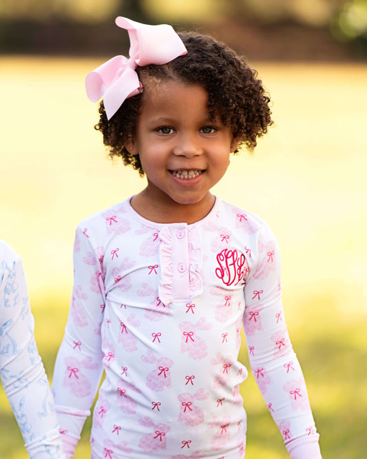 Young girl wearing a white long-sleeve shirt with pink bow patterns outdoors.