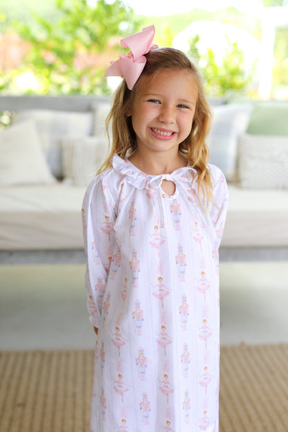 Young girl wearing a white nightgown with nutcrackers and ballet dancers, standing outdoors.