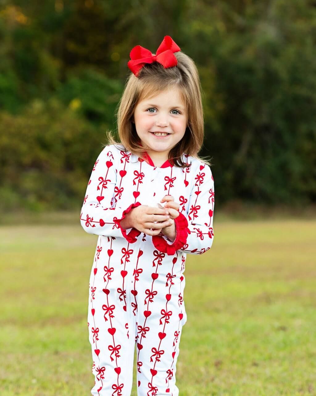 Young girl wearing a white onesie with red patterns outdoors.
