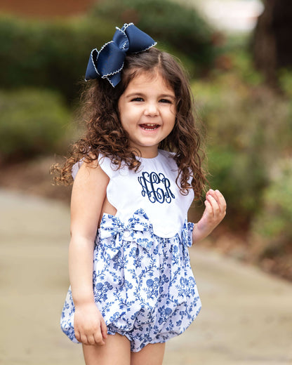 Young girl wearing a white top with 'LOR' monogram and a blue floral dress, outdoors.