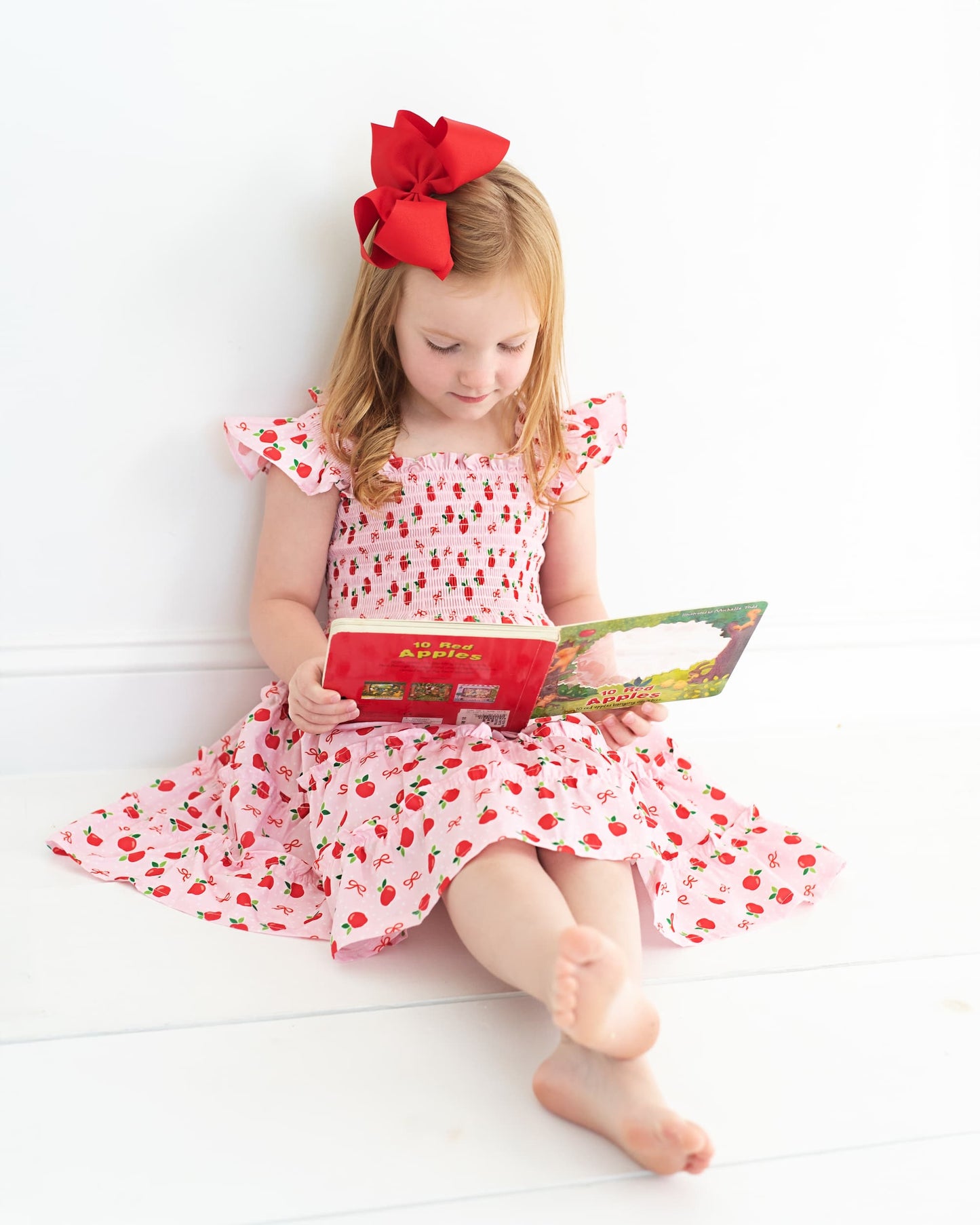 Young girl wearing an apple print dress sitting down reading a book.