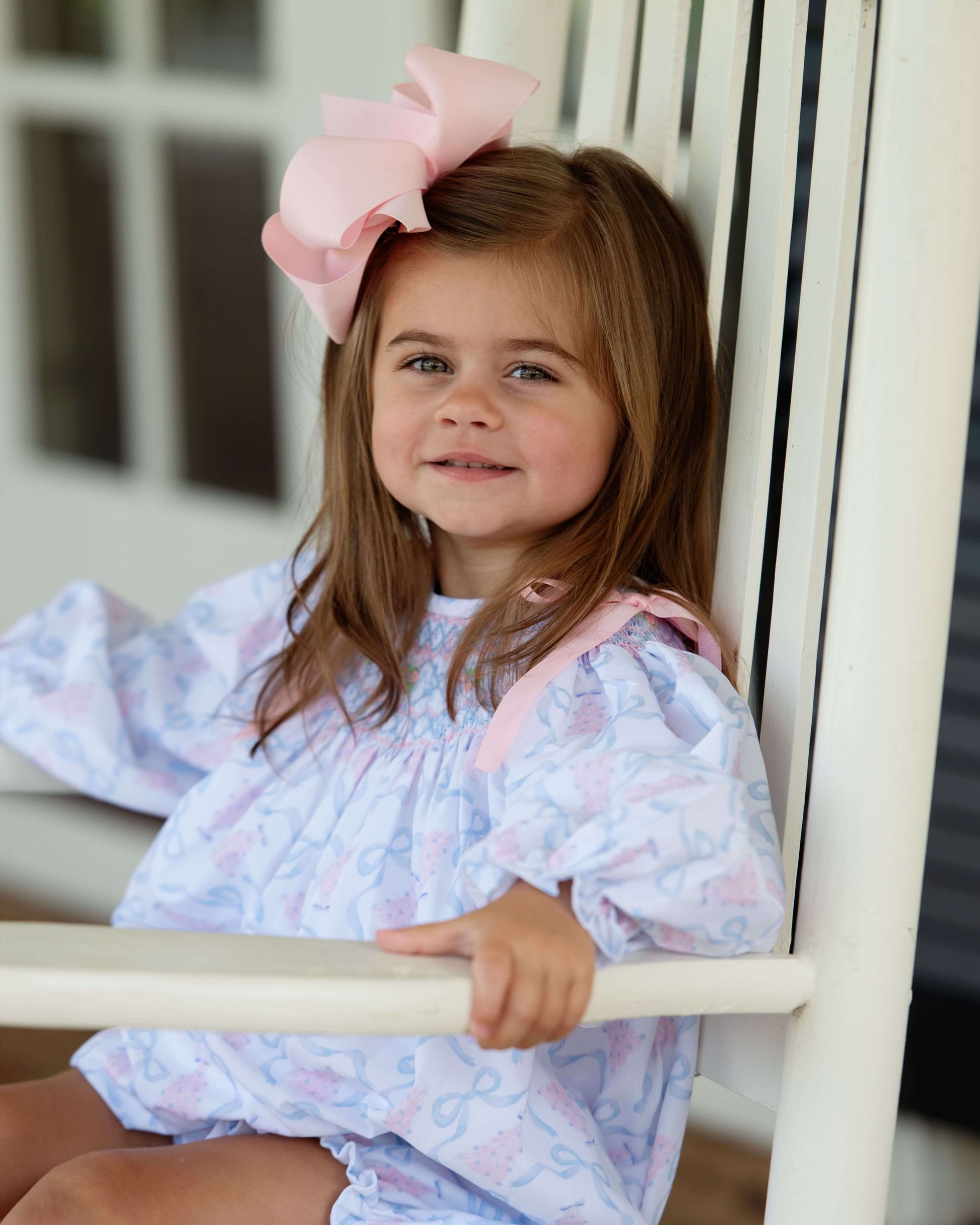 Young girl with a large pink bow in her hair, wearing a light-colored Christmas outfit.
