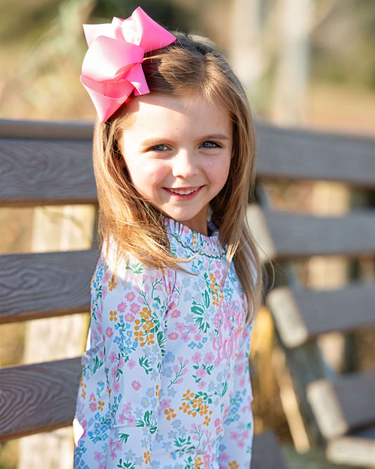 Young girl with a pink bow in her hair, wearing a floral dress, standing outdoors.