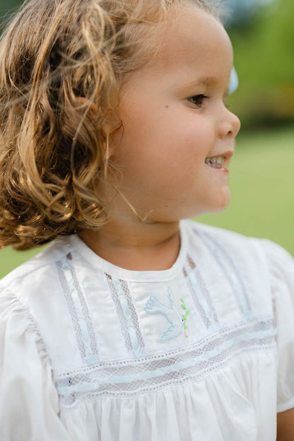Young girl with curly hair wearing a white bubble with lace details, standing outdoors.