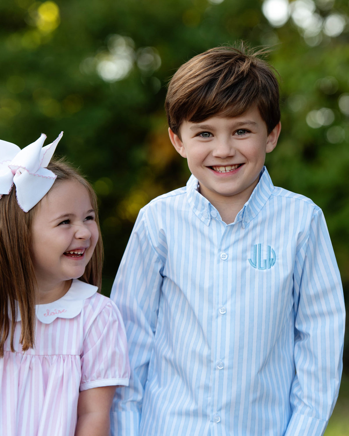 boy and girl standing outside smiling, wearing pink and blue striped outfits