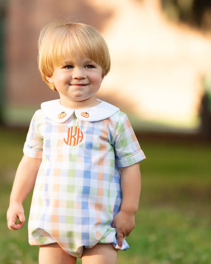 boy wearing a checkered romper with a monogram "jKh", standing outdoors.