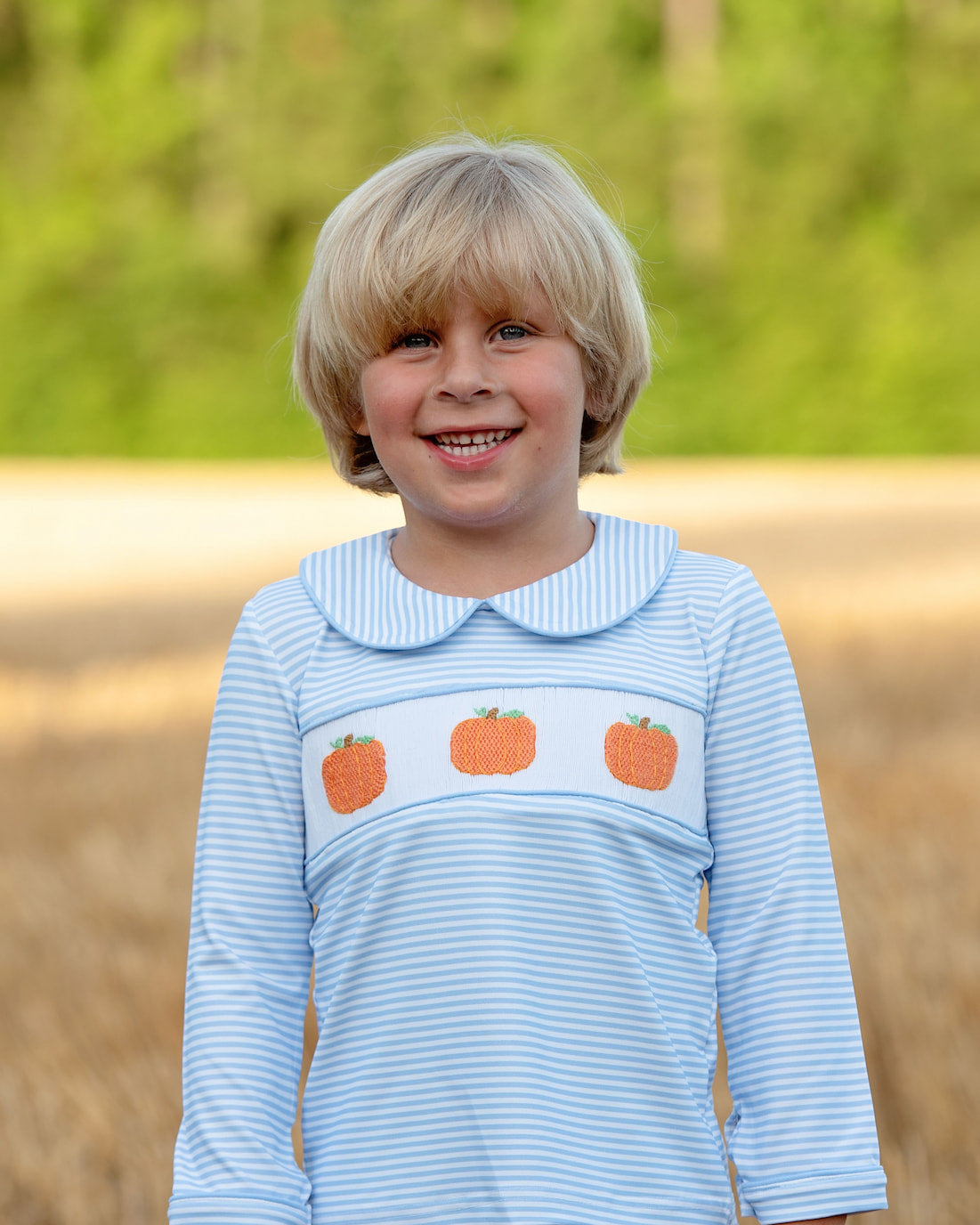 Child wearing a blue striped shirt with pumpkin design outdoors
