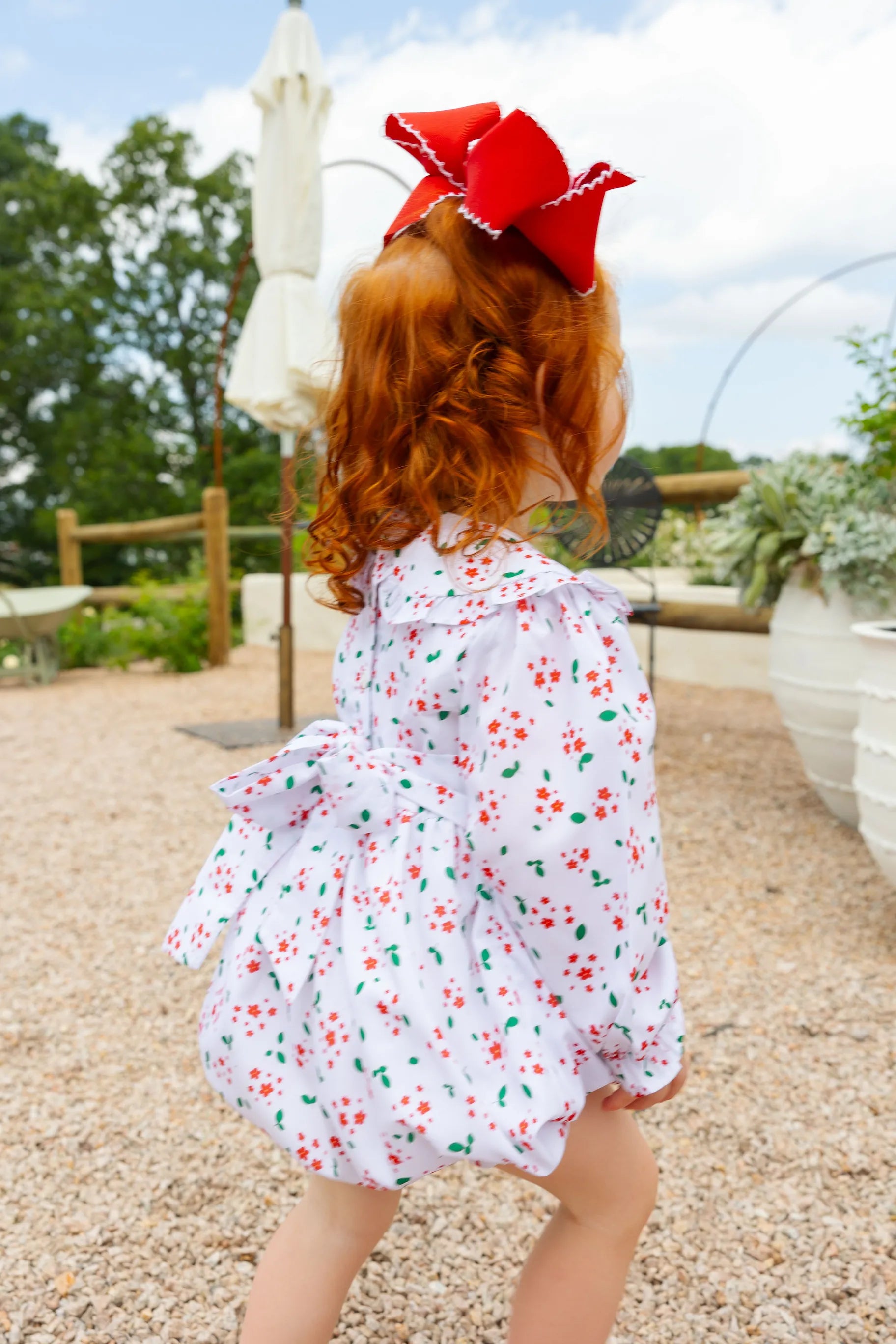 Child wearing a floral dress with a red bow in an outdoor setting