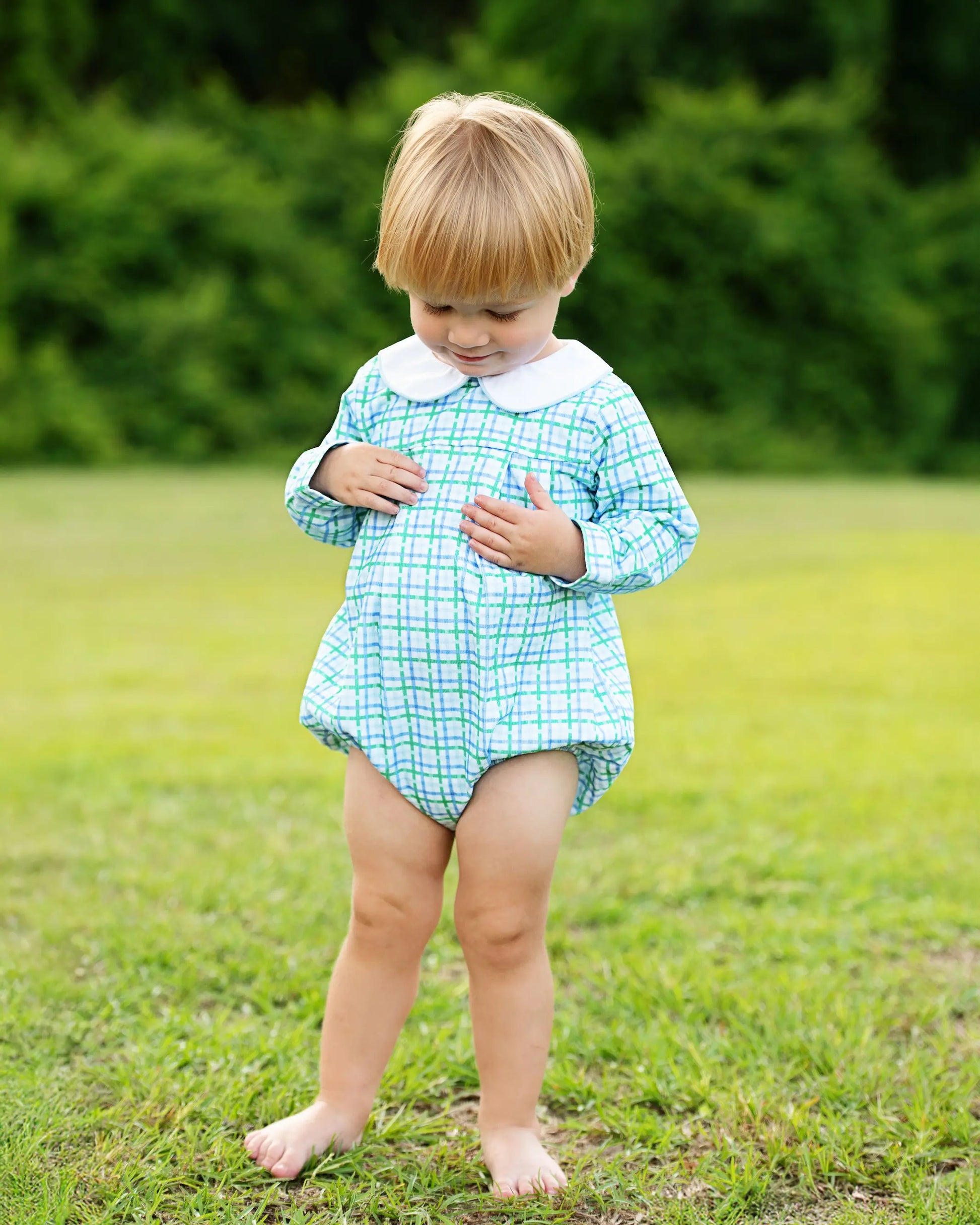 Child wearing a green checkered dress standing in a grassy field