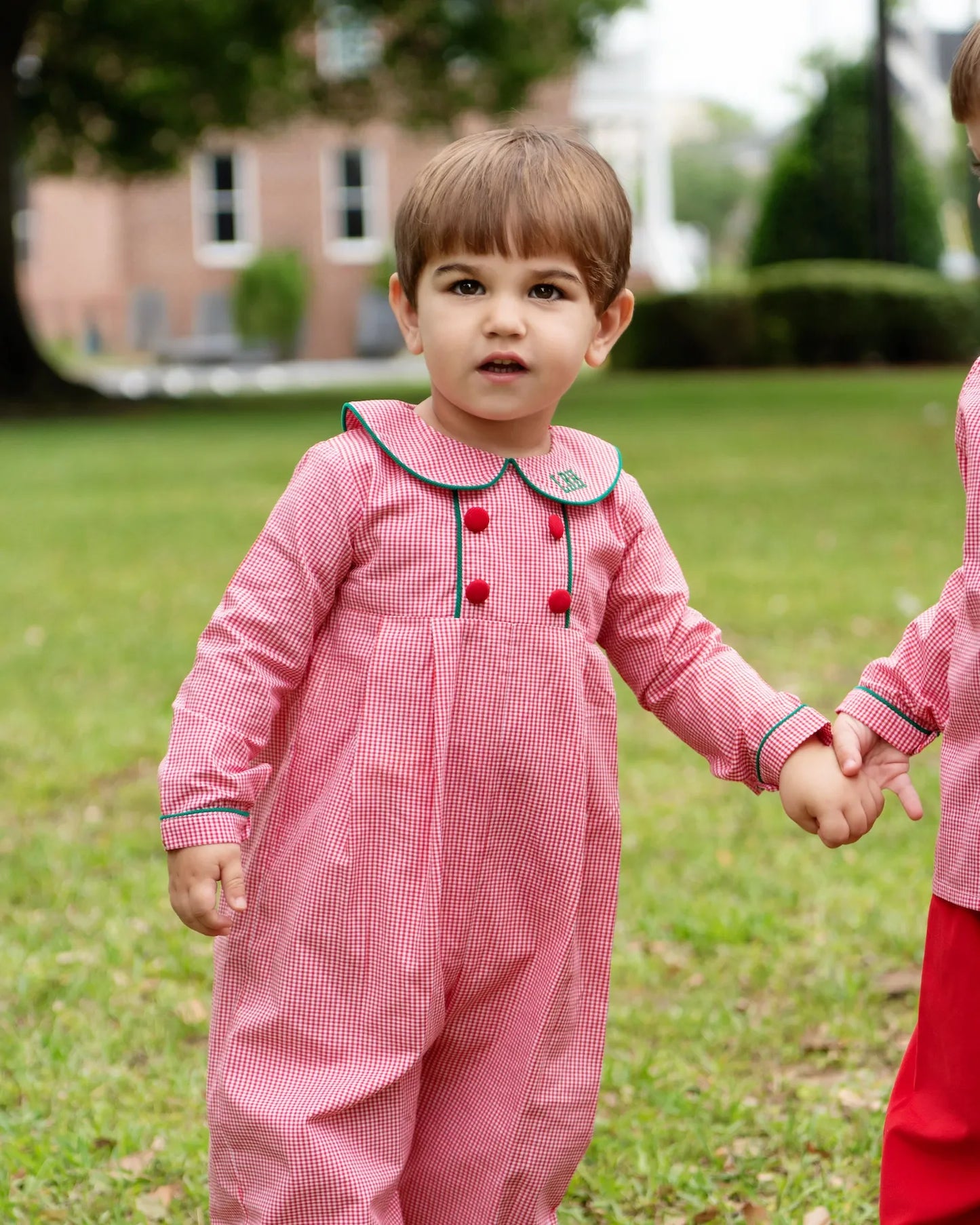 Child wearing a pink outfit with red buttons outdoors on a grassy area.