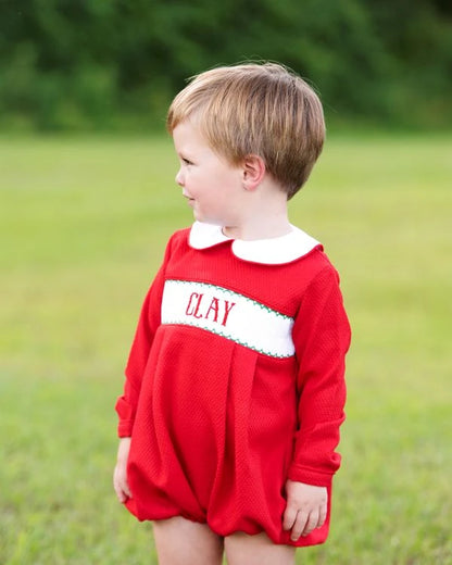 Child wearing a red dress with 'CLAY' printed on it, standing in a grassy field.