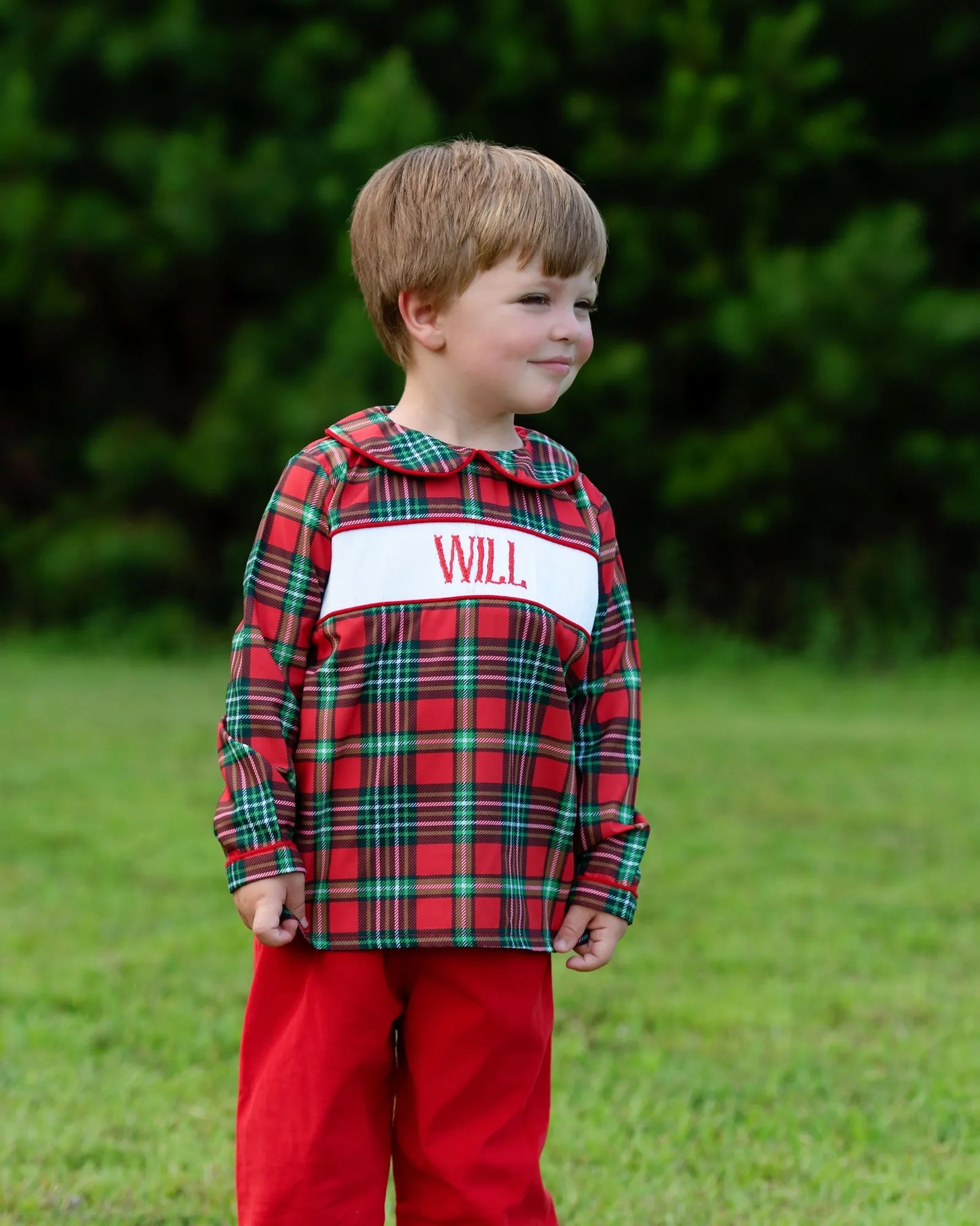 Child wearing a red plaid shirt with 'WILL' on it, standing outdoors.