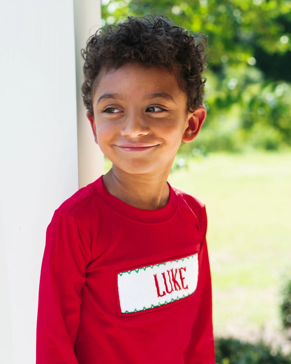 Child wearing a red custom smocked shirt personalized with a name, outdoors