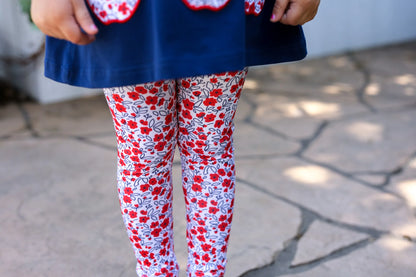 Child wearing red floral leggings with a blue top on a stone pavement.