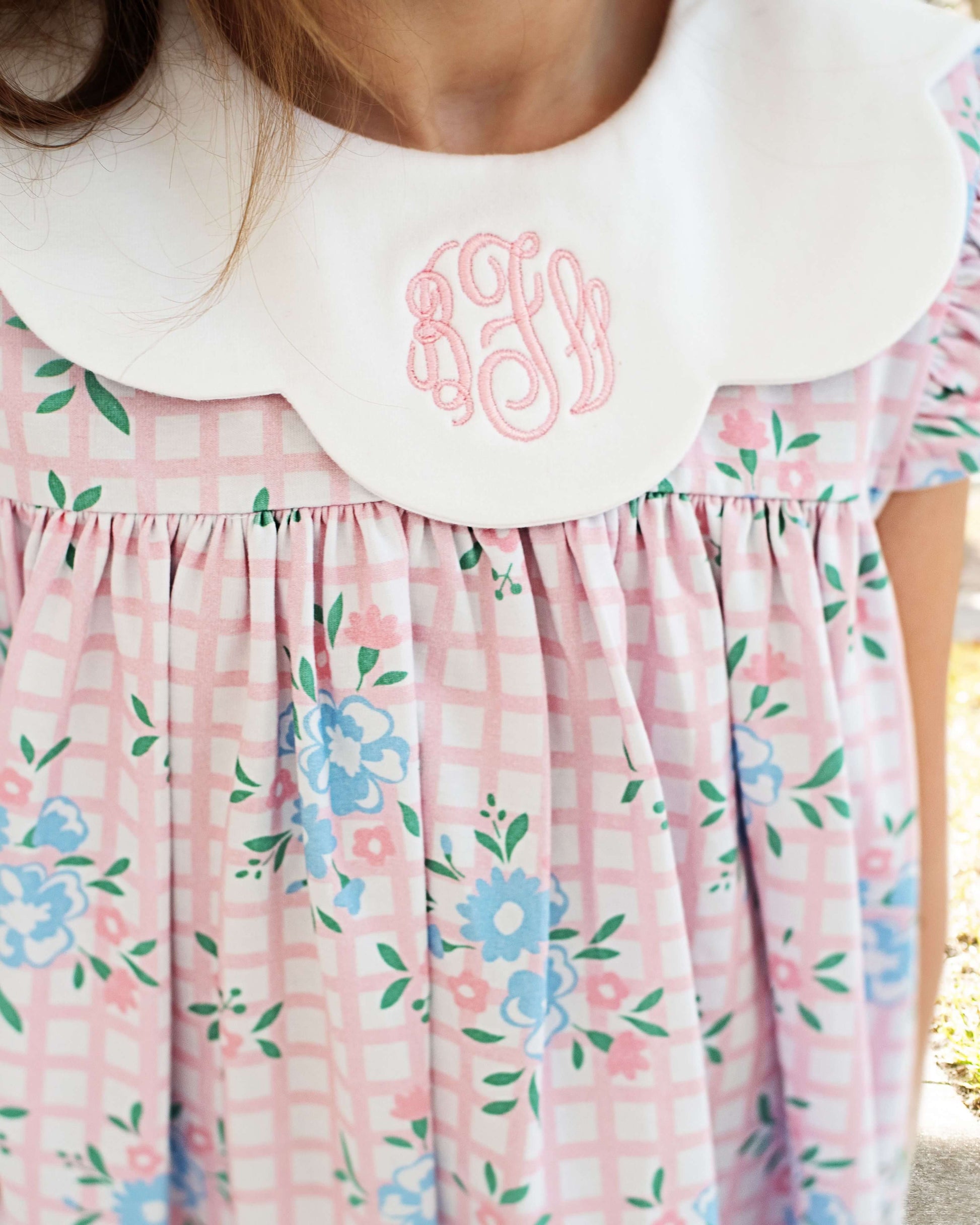 close up of a floral dress with pink letters monogrammed on the scalloped collar