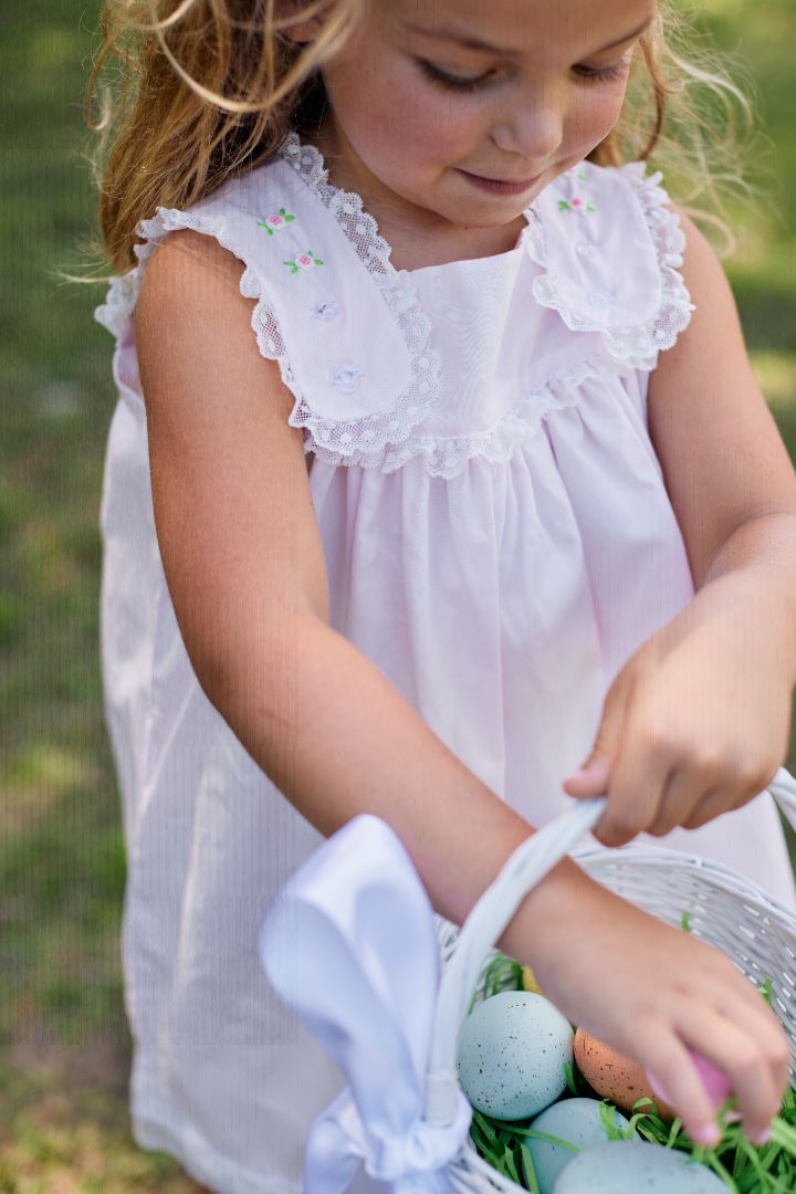 Close-up of pink dress bodice showing embroidered rosebud detail and white lace trim