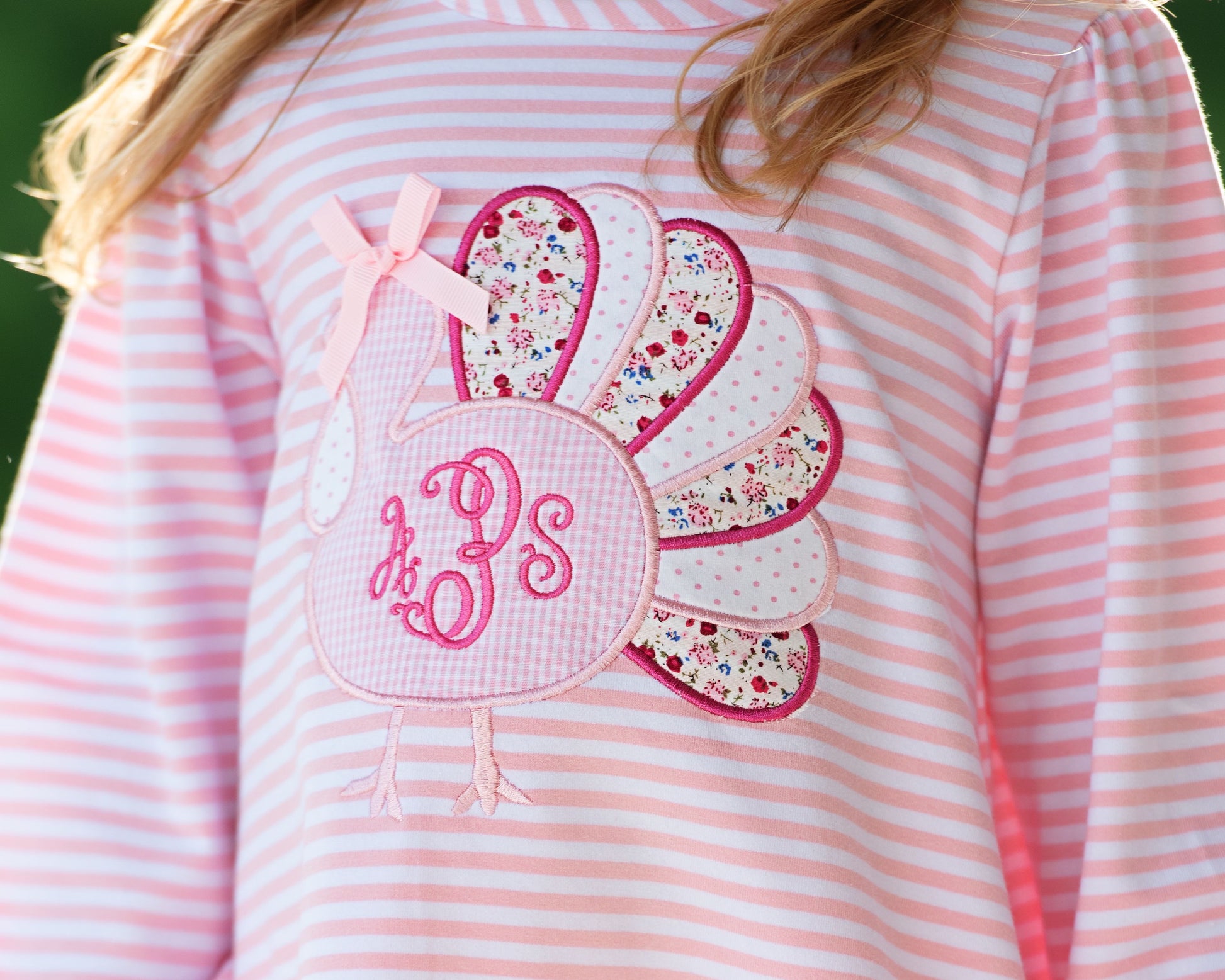 close up of pink and white striped legging set with floral turkey and monogram "aPs'  on a blurred green background