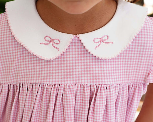 closeup of pink embroidered bows on a white scalloped collar and pink gingham