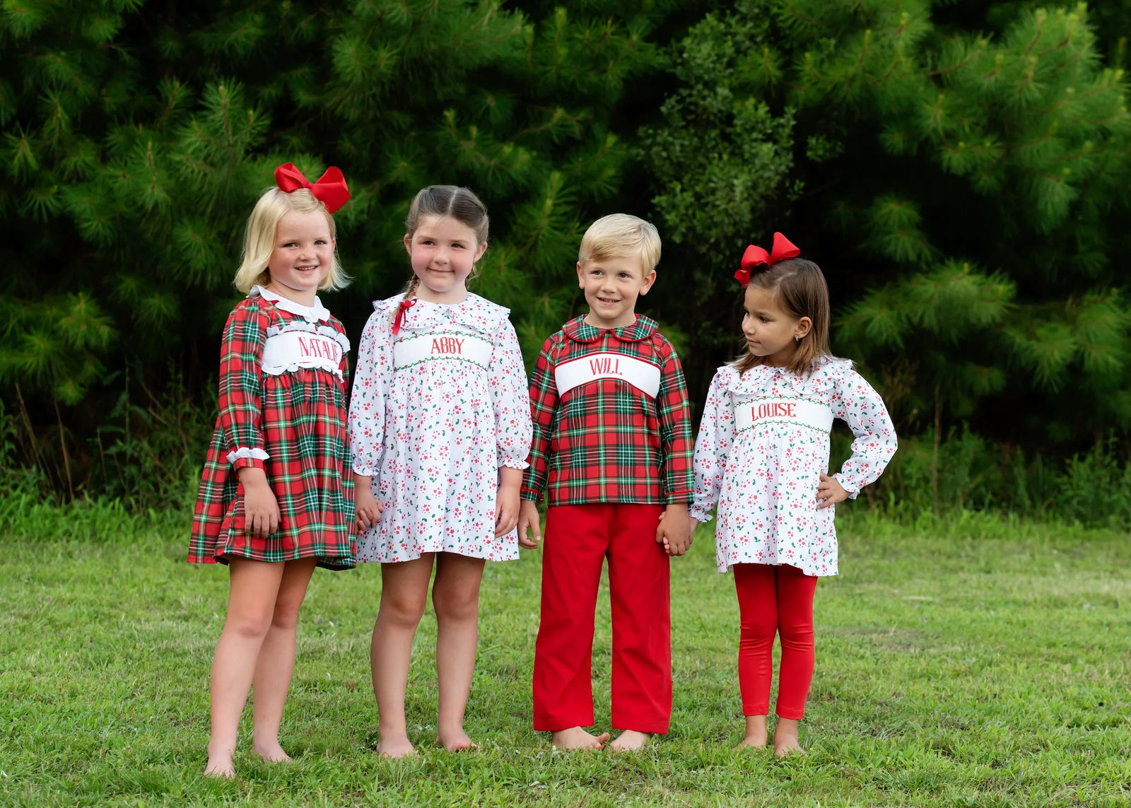 Four children in matching red and green plaid custom smocked outfits outdoors