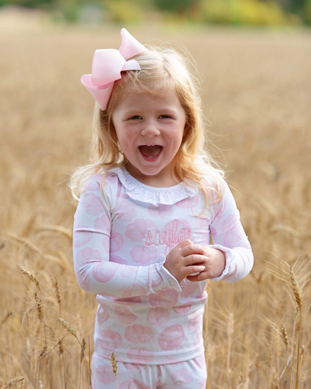 girl in a pink pajama set with a bow standing in a field of tall grass.