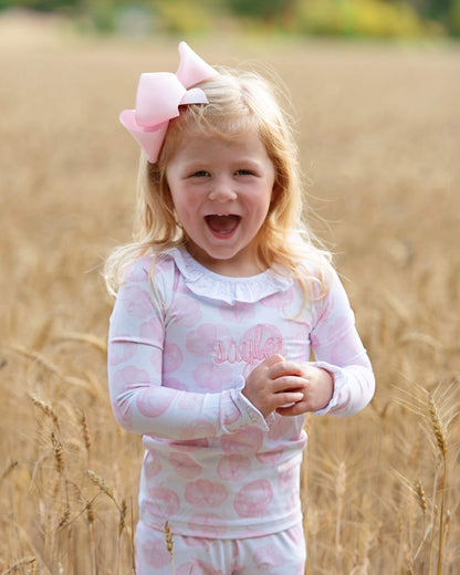 girl in a pink pajama set with a bow standing in a field of tall grass.