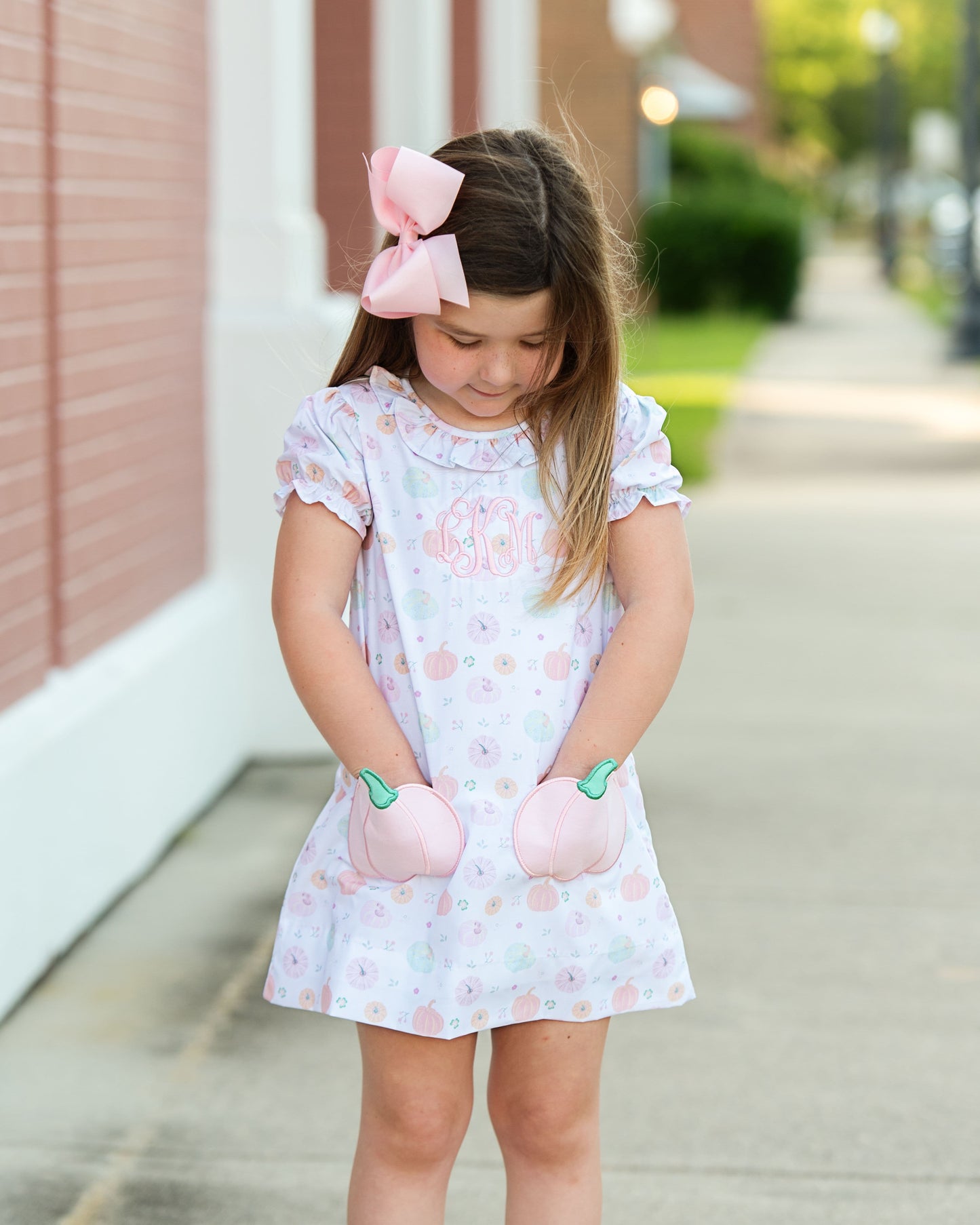 girl in a pumpkin dress with bow  standing on a sidewalk.