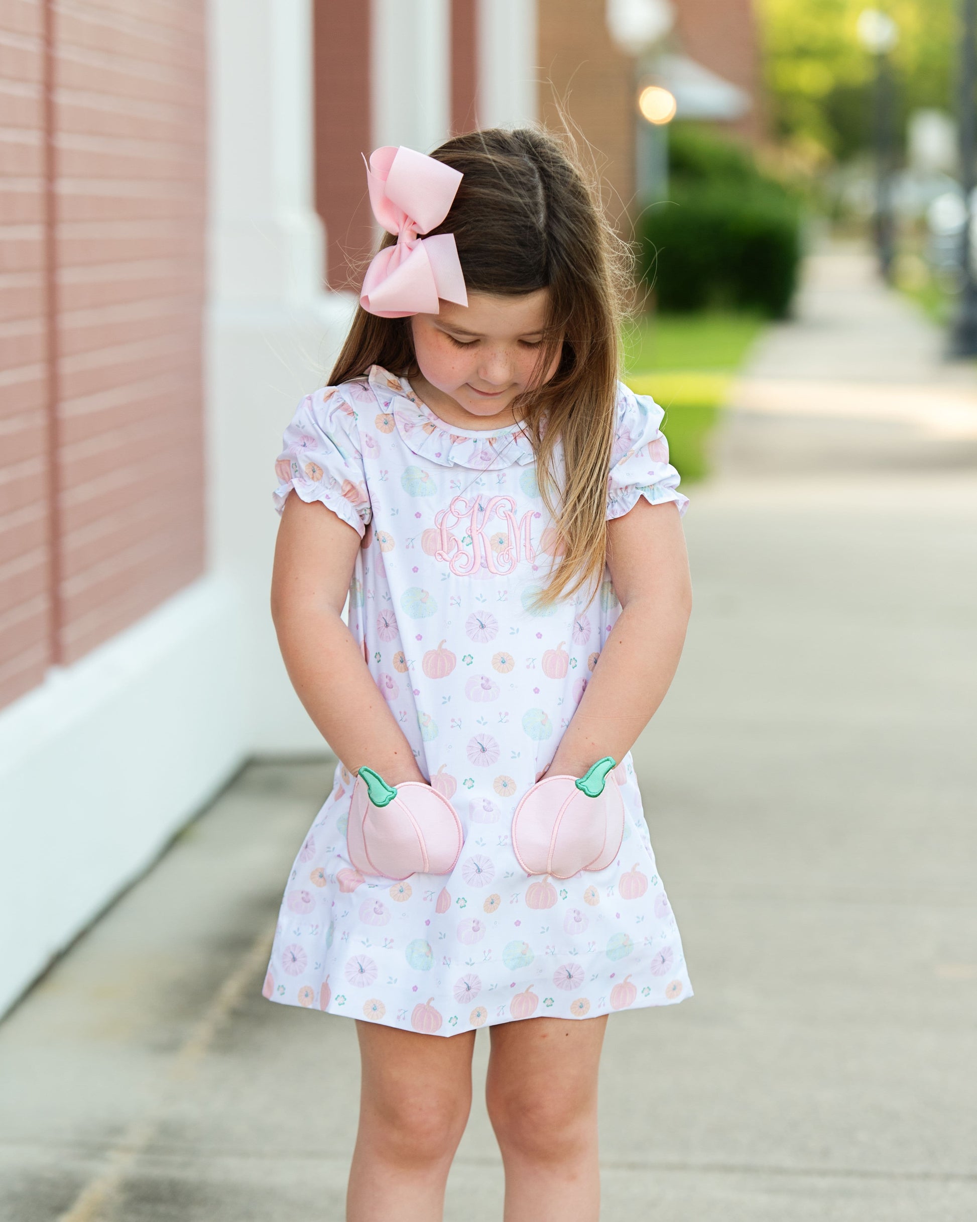 girl in a pumpkin dress with bow  standing on a sidewalk.