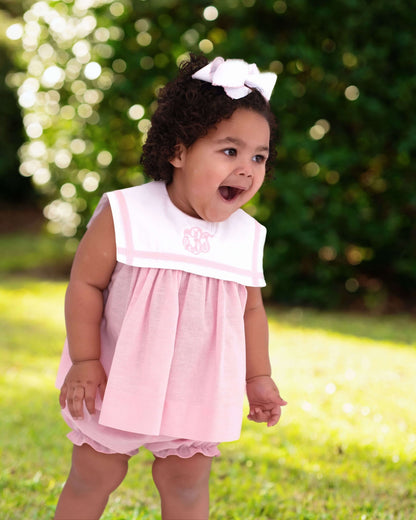 girl wearing a pink outfit with a monogram and greenery in the background