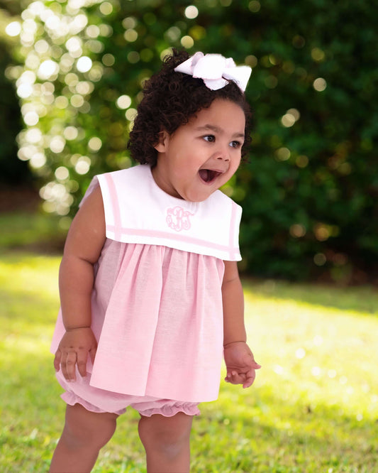 girl wearing a pink outfit with a monogram and greenery in the background