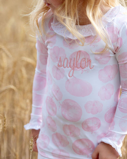 girl wearing a pink pumpkin pajama set with 'saylor' monogram, standing in a field.