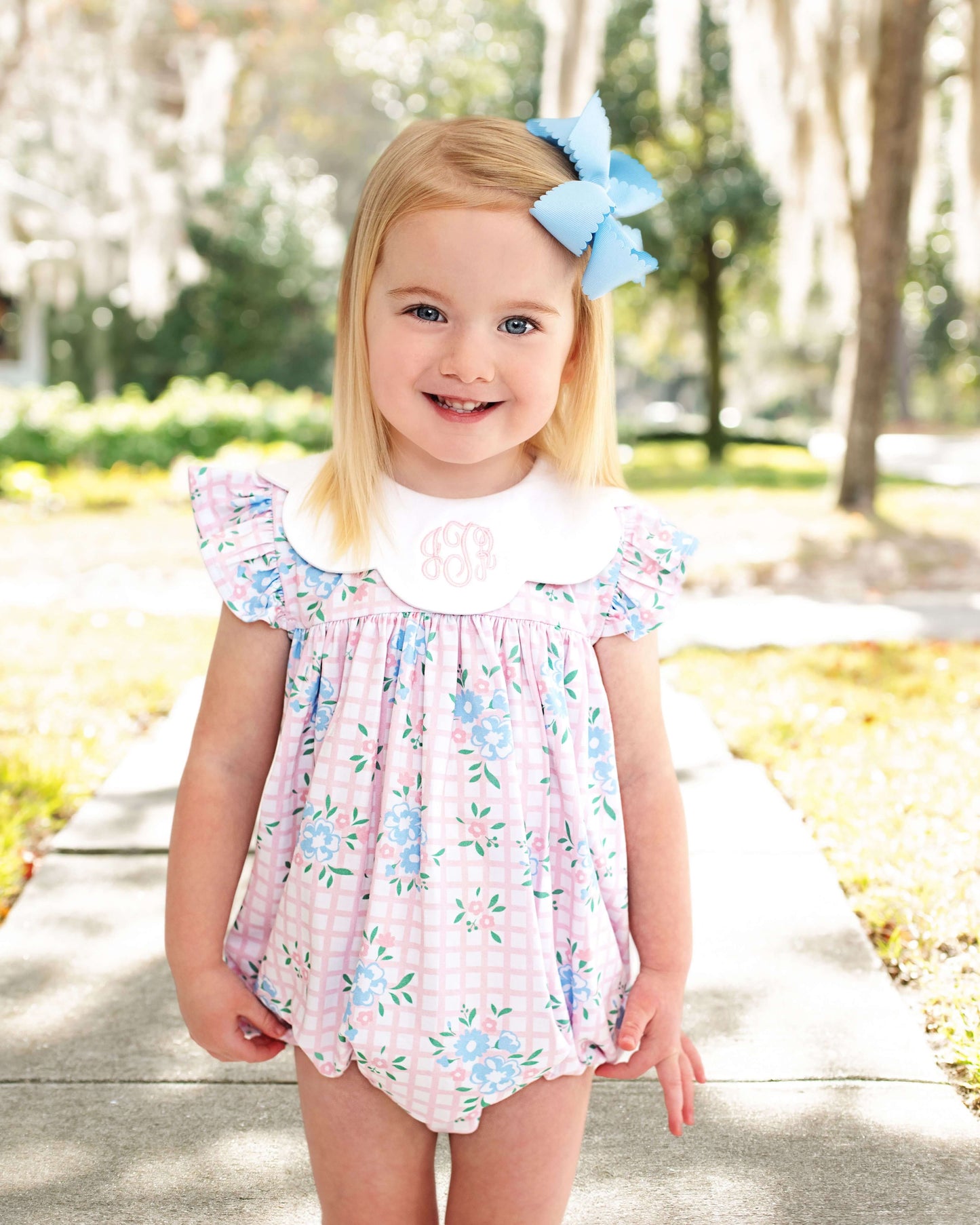 little girl modeling a floral bubble standing outside with a blue bow in her hair