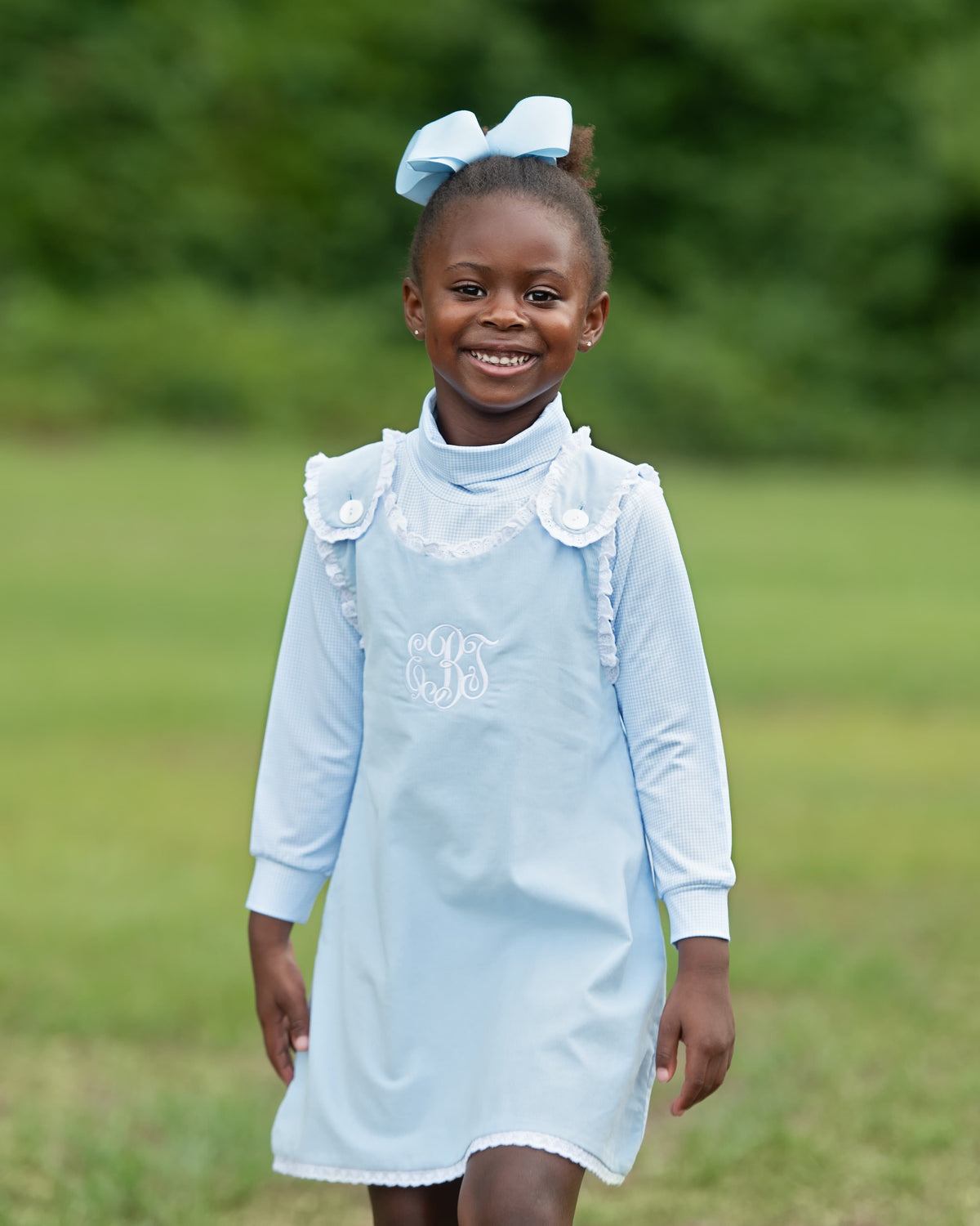 little girl standing in a field wearing a blue corduroy dress set with a matching blue bow